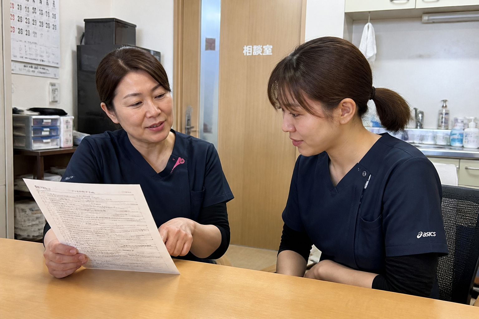 先輩看護師が若手看護師にCVポート管理のチェックリストを説明している様子