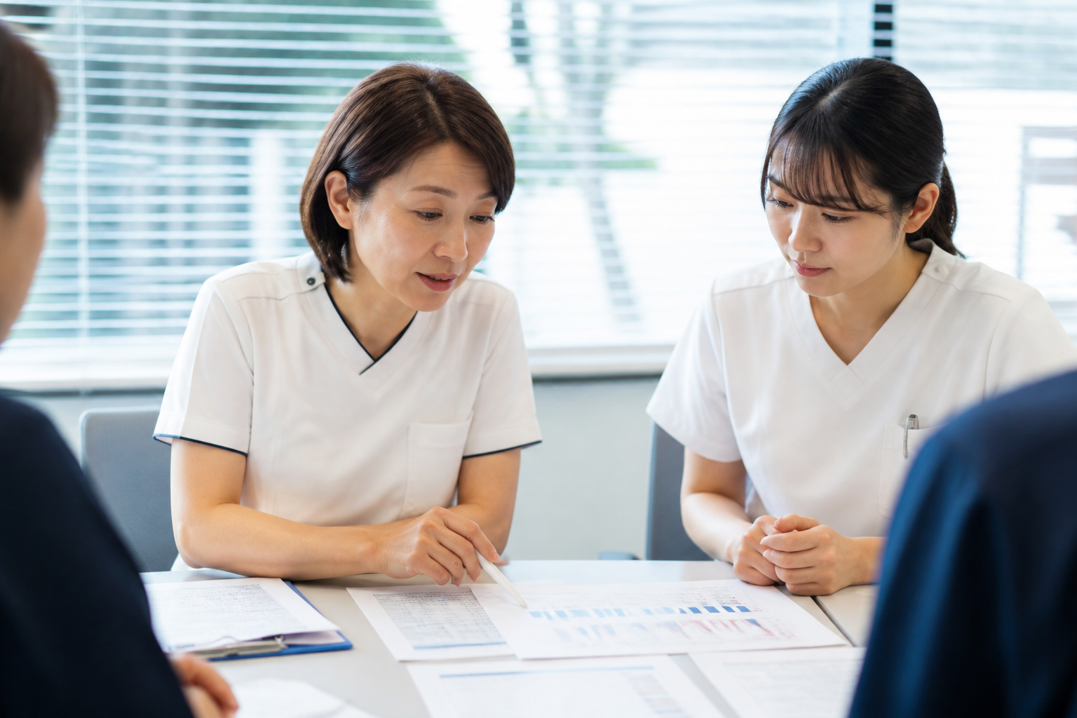 残業時間の統計資料を見比べる日本人の看護管理者と看護師