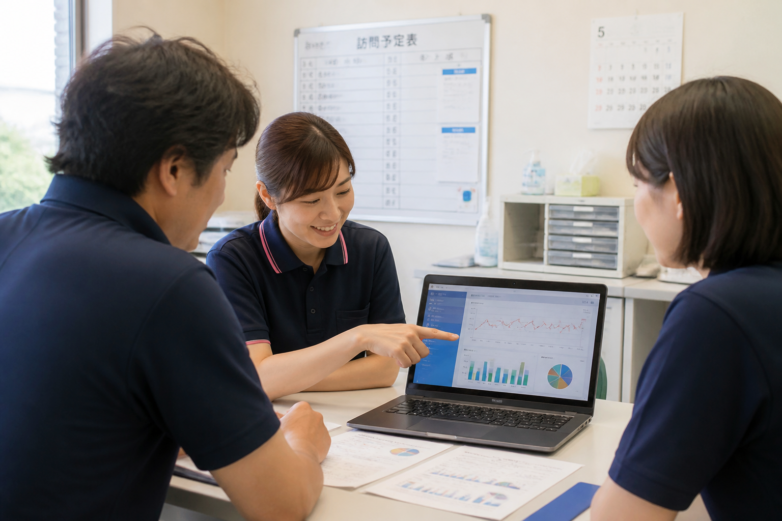 訪問看護ステーションで需要データを確認しながら打ち合わせをする日本人スタッフの様子