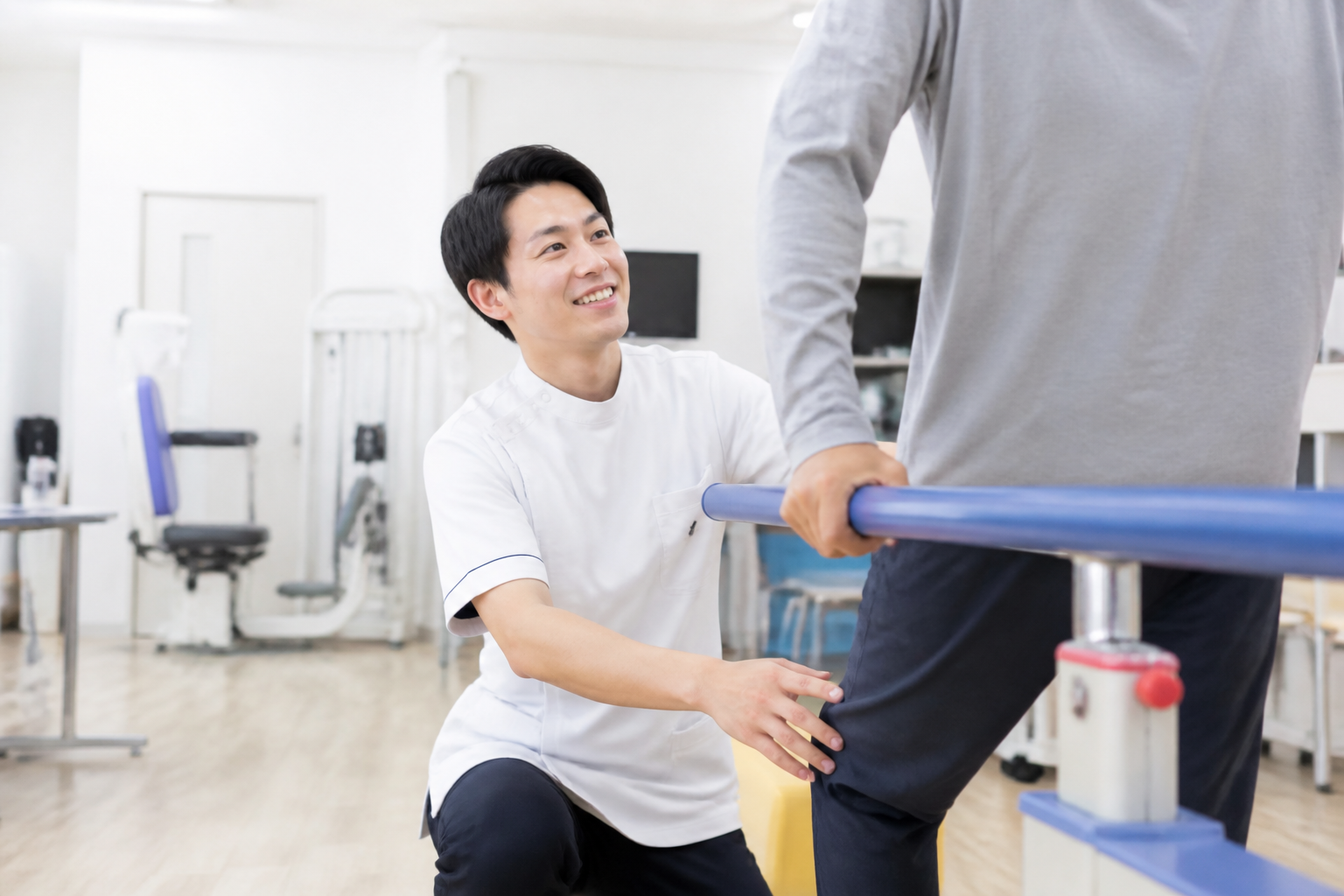 病院のリハビリ室で患者の歩行訓練をサポートする日本人理学療法士